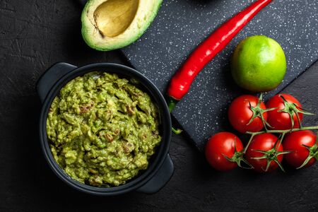 Bowl of guacamole with fresh ingredients on a black table