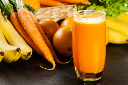Glass of fruit juice with orange, carrots and banana on a tableの写真素材