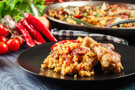 Traditional paella with chicken legs, sausage chorizo and vegetables served on black plate. Spanish cuisineの写真素材
