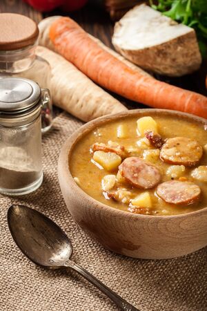 Wooden bowl of split pea soup with sausage, bacon and potatoesの写真素材