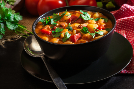 White bean soup with potatoes, tomatoes, paprika, and bacon in black ceramic bowlの写真素材