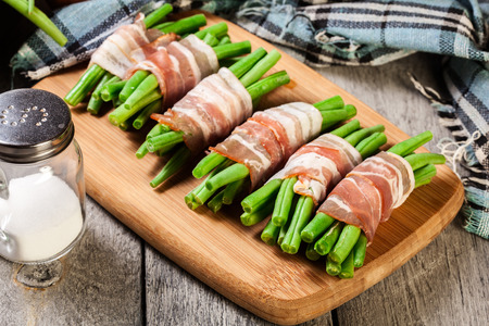 Green bean wrapped in smoked bacon on cutting boardの写真素材