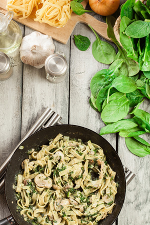 Tagliatelle pasta with spinach and mushrooms on a pan. Vegetarian food. Top viewの写真素材