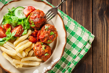 Roasted meatballs in tomato sauce with french fries and salad on a plate. Top viewの写真素材