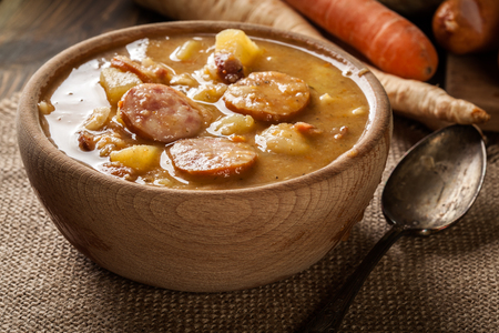 Wooden bowl of split pea soup with sausage, bacon and potatoesの写真素材