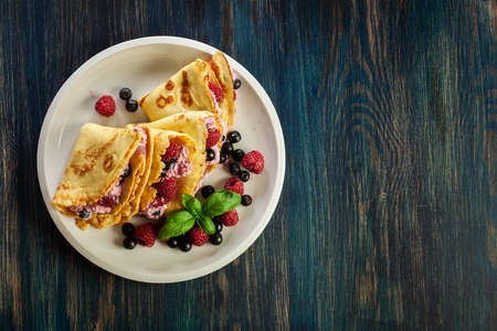 Delicious tasty homemade traditional crepes with cottage cheese, raspberries, and chokeberry. Top viewの写真素材
