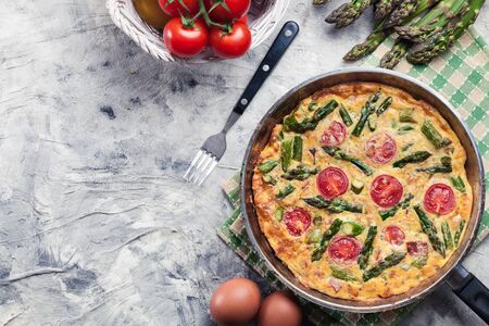 Frittata made of eggs, asparagus and cherry tomatoes on a frying pan. Italian cuisineの写真素材