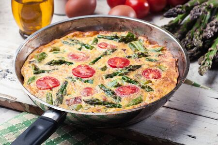 Frittata made of eggs, asparagus and cherry tomatoes on a frying pan. Italian cuisineの写真素材