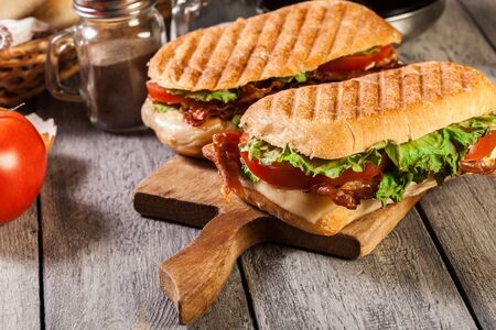Toasted ciabatta sandwich with smoked bacon, cheese and tomato on cutting board