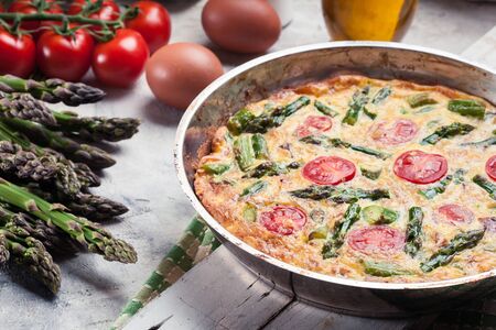 Frittata made of eggs, asparagus and cherry tomatoes on a frying pan. Italian cuisineの写真素材
