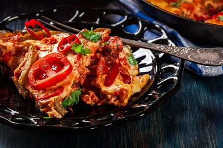 Portion of frittata with eggs, sausage chorizo, red pepper, green pepper, tomatoes, cheese and chili in a plate on wooden table. Italy cuisineの写真素材