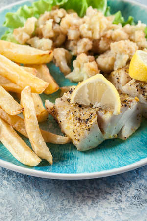 Steamed cod fish with french fries and boiled cauliflower on a plateの写真素材