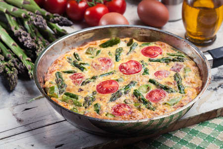 Frittata made of eggs, asparagus and cherry tomatoes on a frying pan. Italian cuisineの写真素材