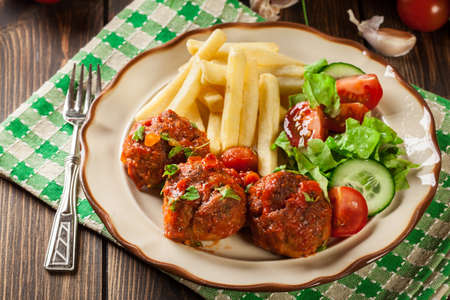 Roasted meatballs in tomato sauce with french fries and salad on a plateの写真素材