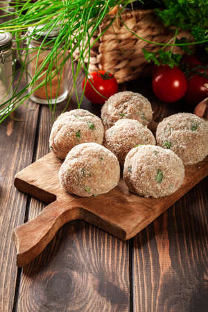 Raw meatballs rolled in a crispy bun on a chopping board prepared for bakingの写真素材