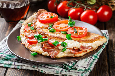 Omelette with bacon and tomatoes on brown plate.の写真素材