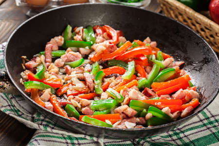 Frieding ingredients for preparing omelette with bacon and bell pepper on panの写真素材
