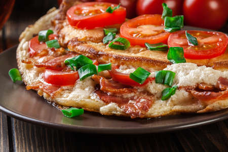 Omelette with bacon and tomatoes on brown plate.の写真素材