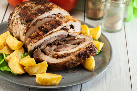 Roasted pork roll stuffed with other meat and dried tomatoes served with fried potatoesの写真素材