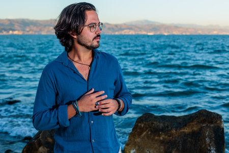 very attractive young man with blue shirt and white pants posing on the beach with the sea in the backgroundの写真素材