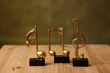 Three golden music notes statuettes standing on a wooden surface are representing musicの写真素材