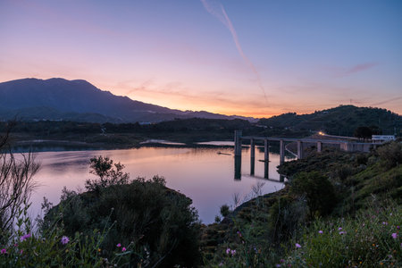 Calm water reflecting colorful sunset sky over mountains and bridge at Guadalhorce reservoir in Malaga, Spainの写真素材