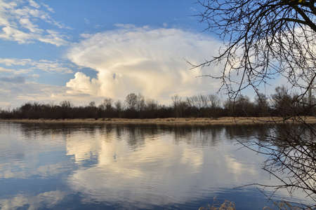 Overgrown river bank and clouds in the sky on a spring day. Clouds and water.