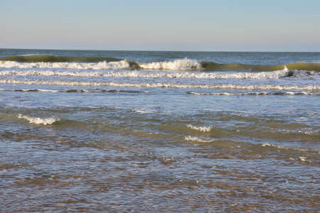 The shore of the sea at low tide, visible sea waves in the distance. Spring.