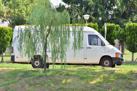 A white delivery truck is behind the trees. Summer.の写真素材