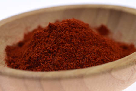 Red ground paprika on a wooden bowl against a white background. Spices.