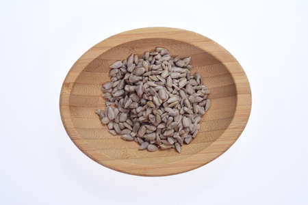 Shelled sunflower seeds on a wooden bowl against a white background. Food.の写真素材