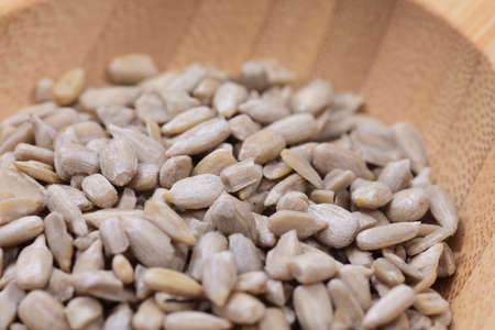 Shelled sunflower seeds on a wooden bowl against a white background. Food.