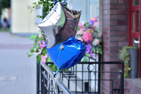 A silver and blue balloon tied to a metal railing against the background of traffic. Bokeh.の写真素材