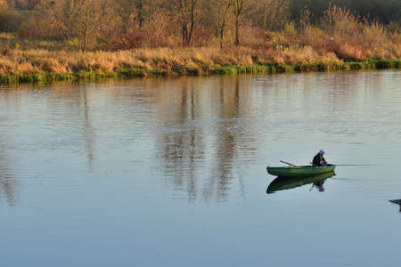 A lone angler on a boat in the middle of the river on a quiet day.の写真素材