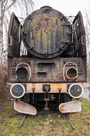 An old and dilapidated historic PKP steam locomotive standing on a siding on a gloomy autumn day.