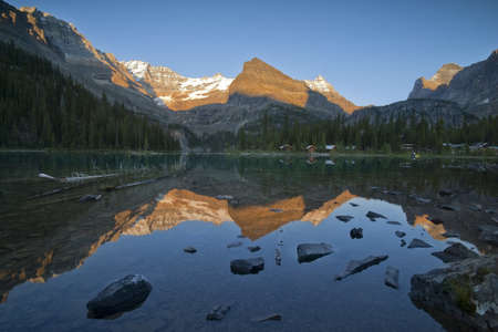 mountain tops around lake ohara glowing in sunset light, reflection in lake and tourist cabins on lakeshore の写真素材
