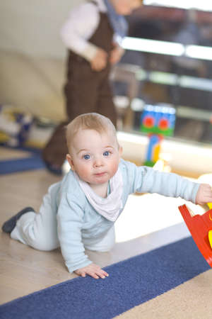 baby boy playing on floor with brother in backgroundの写真素材