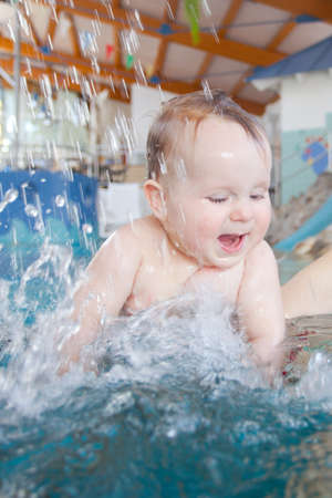 baby standing under shower in swimming pool indoorsの写真素材