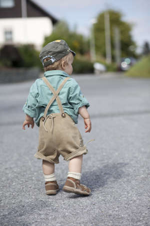 boy in traditional lederhosen walking on street in residential area, seen from behindの写真素材
