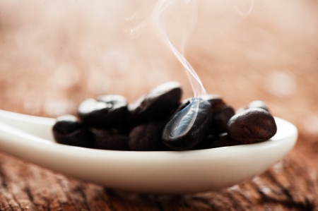 Freshly roasted coffee beans in a white spoon on a wooden  tableの写真素材