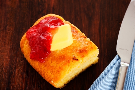 A piece of butter cake with butter and strawberry jam on a wooden plate