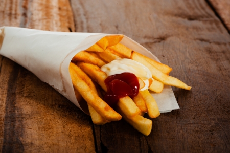 Potatoes fries in a little white paper bag with ketchup and mayonnais on wood boardの写真素材