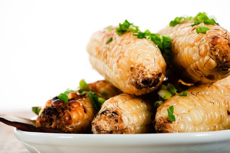 Barbecued corn cobs with herbs on a white plate and a wooden tableの写真素材