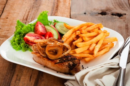 A menu with meat french potatoes roasted onion and salad on white plateの写真素材