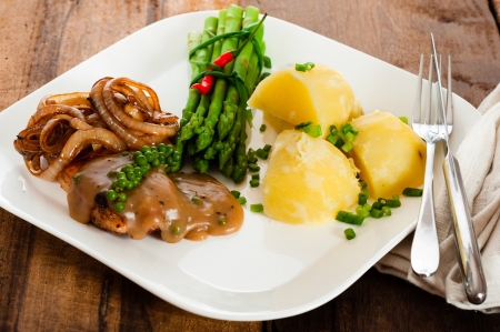 Freshly prepared piece of meat with onions and pepper sauce, cooked potatoes green asparagus and green pepper as a decoration on a white plate の写真素材