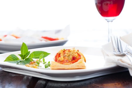 A small piece of mini pizza with some herbs on white plate and a glass of red wine in the backgroundの写真素材