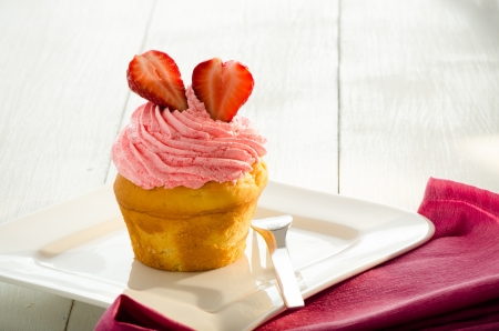 strawberry cupcake and two fresh strawberry on the top. White plate and forkの写真素材
