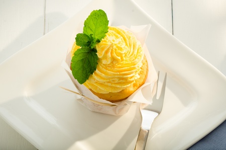 cupcake with yellow cream and fresh mint leaves as decoration on white plateの写真素材