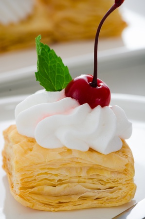 puff pastry cake with cream cherry and fresh mint leaf on white plateの写真素材