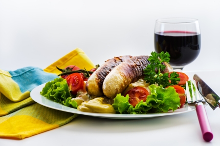 Sausage and green salad plate with tomatoes ripe on white plate and a glass of red wineの写真素材